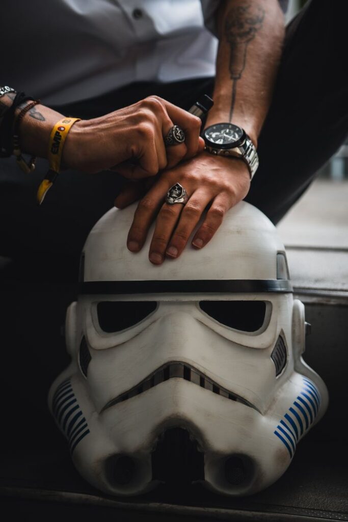 Close-up of hands with rings resting on a Stormtrooper helmet, capturing a moody and stylish vibe.